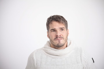 Obraz premium Sad facial expression of a man in a white sweater in front of a white background