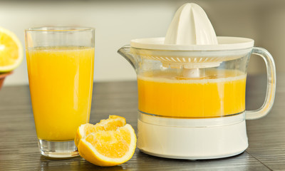 White juicer with glass of freshly squeezed orange juice  background.