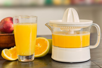 Glass and juicer with freshly squeezed orange juice with bowl of fruits on the background.