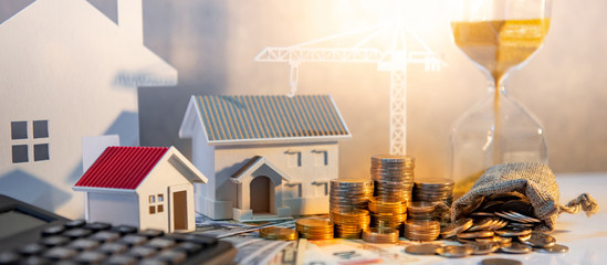 Real estate or property development. Construction business investment concept. Home mortgage loan rate. Coin stack on international banknotes with calculator, house and crane models on the table. - obrazy, fototapety, plakaty