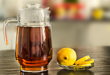 Glass pitcher with hot black tea with lemons on kitchen background.