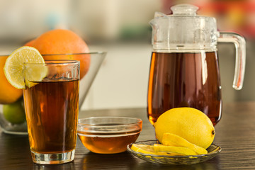 Pitcher with glass of hot black tea with bowl of honey and fruits  and lemons on kitchen background.