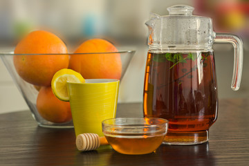 Pitcher and cup of hot black tea with mint, honey and lemons  the  background.