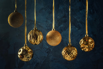Fototapeta na wymiar Copy space on a dark blue background with decorative putty textures. Six golden christmas balls hanging on ribbons. Festive layout.