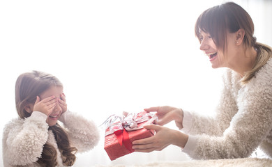 Christmas concept, Mom gives a gift to a little cute daughter, a place to text on a light background