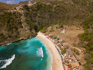 Aerial view to beautiful Atuh beach with buildings, sunbeds and hindu temple. Turquoise ocean water. Photo from drone. Nusa Penida, Bali, Indonesia