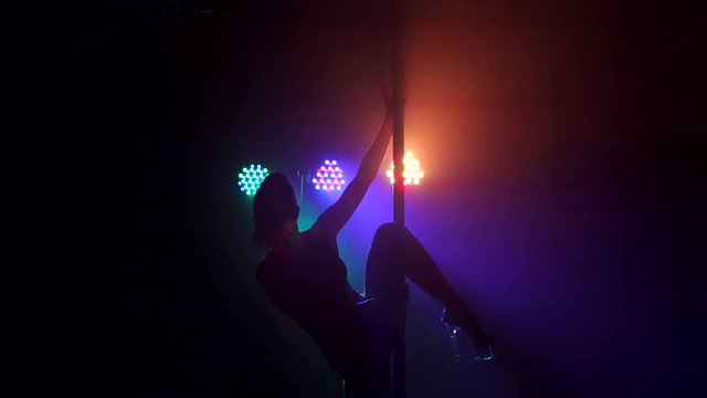 Silhouette of a sexy girl who does a complex exercise on a pylon in the dark. Slow motion.