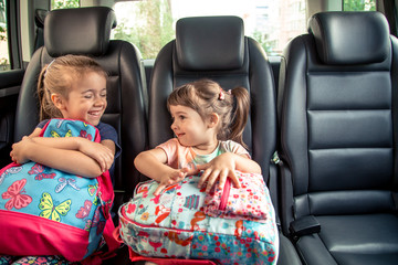 Children in the car go to school, happy, sweet faces of sisters