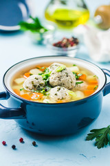 Meatball vegetable soup in a pot on light blue background. Selective focus, space for text.