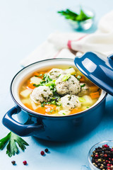Meatball vegetable soup in a pot on light blue background. Selective focus, space for text.