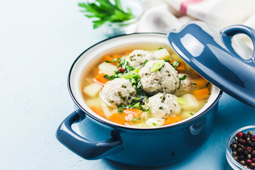 Meatball vegetable soup in a pot on light blue background. Selective focus, space for text.
