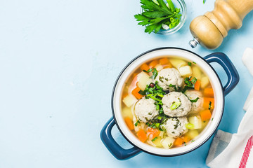 Meatball vegetable soup in a pot on light blue background. Top view, space for text.