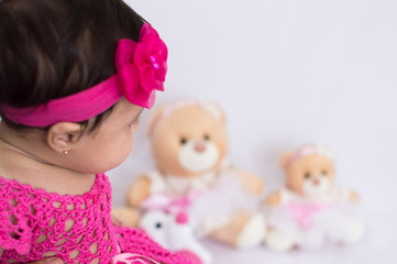 Fototapeta na wymiar Baby with pink dress looking at the teddy bears blurred in the background