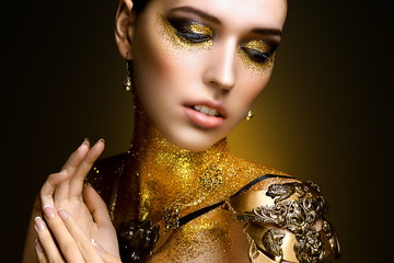 Portrait of beautiful woman with golden glitter on her body. Fashion model with art make-up with...