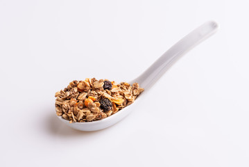 Granola or muesli with nuts and rasins in a white spoon on a white background, angle view, soft light