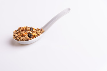 Granola or muesli with nuts and rasins in a white spoon on a white background, angle view, copy space, soft light