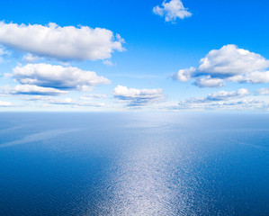 Aerial view of a blue sea water background and sun reflections. Aerial flying drone view. Waves water surface texture on sunny tropical ocean. Aerial photography. Birdseye. Sea, beach, sky, clouds.