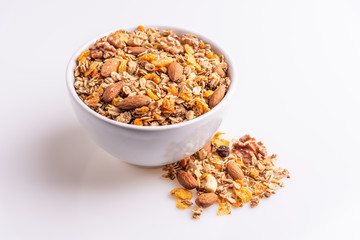 Granola or muesli with nuts and rasins in a white bowl on a white background, angle view, soft light