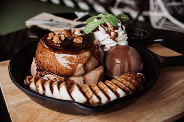 Delicious pancake with banana chocolate and vanilla ice cream on black iron pan over cock coaster.