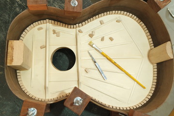 Luthier gluing parts harmonica structure top with brush and tweezers of a classical guitar