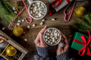 Girl drinks hot chocolate with marshmallow, cocoa mug in woman hand in warm winter sweater, old wooden table  with christmas decorations top view copy space