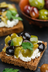 Rye bread toast (canape) with black and green olives, feta cheese and parsley. Tasty snack for gourmets on a slate plate