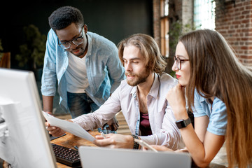 Group of young multi ethnicity coworkers dressed casually working together with computers and documents at the modern office interior