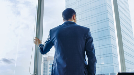 Low Angle Following Shot of the Confident Businessman in a Suit Standing in His Office and Looking out of the Window Thoughtfully. Stylish Modern Business Office with Big City View.
