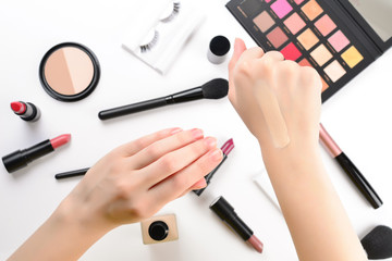 Foundation in woman hands. Professional makeup products with cosmetic beauty products, foundation, lipstick,  eye shadows, eye lashes, brushes and tools.