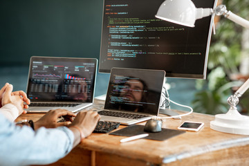 Programmers writing a program code sitting at the workplace with three monitors in the office....