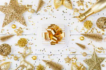 Christmas background with golden gift or present box, champagne and holiday decorations on white table top view. Greeting card. Flat lay style.