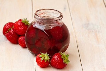Strawberry jam in a jar with fresh strawberries on white wooden background. Glass jar with delicious strawberry confiture. Fresh homemade strawberry jam with berries in small jars, selective focus