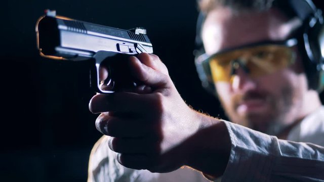 Male shooter holds a gun in a shooting room, close up.