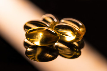 fish oil vitamin d supplement yellow pills on a black glossy background