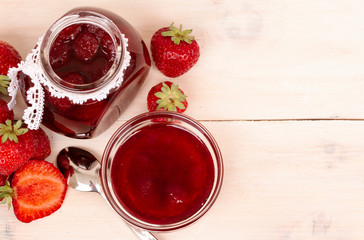 Strawberry jam in a jar with fresh strawberries on white wooden background. Glass jar and bowl with delicious strawberry confiture. Fresh homemade strawberry jam with berries in small jar. top veiw
