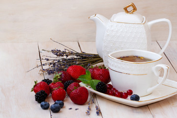 Herbal tea with lavender and mint with fresh strawberries, blackberries and blueberries on a white wooden table. Berry tea with fresh strawberries, blackberries and lavender herb. White porcelain 