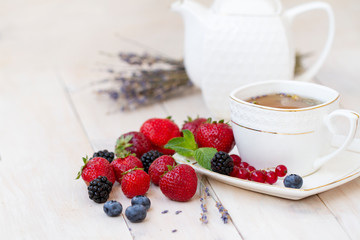 Herbal tea with lavender and mint with fresh strawberries, blackberries and blueberries on a white wooden table. Berry tea with fresh strawberries, blackberries and lavender herb. White porcelain 