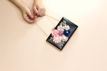 women holding beautiful floral black clutch, wedding bag isolated on pink background