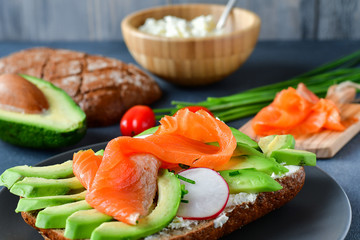 sandwich with avocado and salmon on a dark background, green onions and gluten-free grain bread, radishes and tomatoes, cottage cheese in a wooden plate. concept diet food, vegetarian, copy space