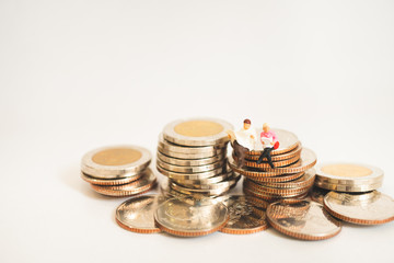 Miniature people man and woman sitting on stack coins isolate on white background using as business and finance concept