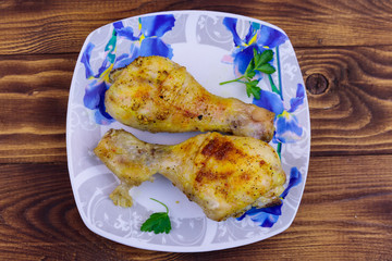 Baked chicken drumsticks with potatoes in a plate on wooden table