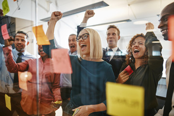 Businesspeople cheering while brainstorming with sticky notes in