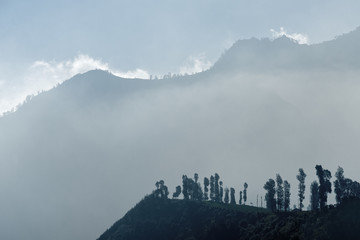 Fototapeta premium In the first morning light view on a mountain chain surrounded by clouds and fog - Location: Indonesia, Java, Mt. Bromo