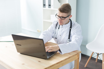 Medicine, working and people concept - doctor sitting at the table and working on laptop