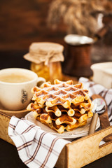 Breakfast with belgian waffles, jam and coffee on tray, rustic background