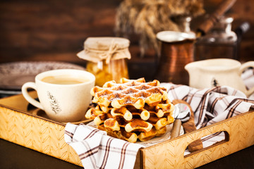 Breakfast with belgian waffles, jam and coffee on tray, rustic background