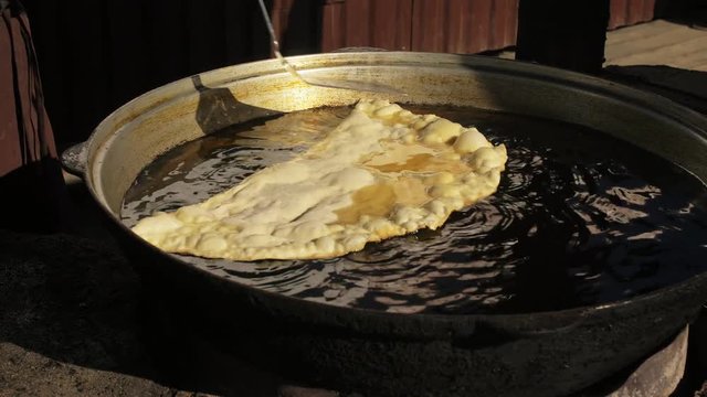 Process cooking national Buryat Mongolian dish cheburek. Big large xxxl 68cm heburek fry with cheese meat onions into cooking pot in oil. Fried flatbread piadina naan pita tortilla shelpek cheburek.