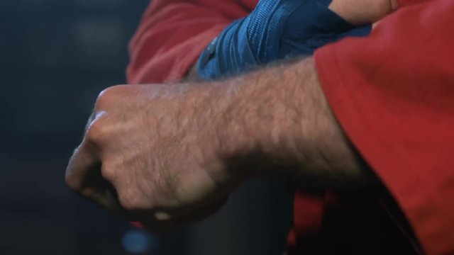 MMA Fighter Prepares For Training. Closeup View Male Wrapping Bandage On Hand. Adult wrestler dressed in red kimono prepare fist for workout indoor in gym. Professional Athlete ready to fight
