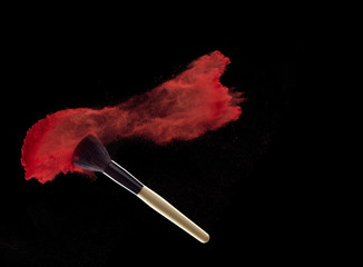 Make-up brush with red powder explosion on black background