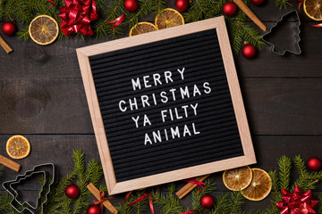 Merry  Christmas Ya Filty Animal letter board on dark rustic wood background with Christmas decoration and fir branch frame top view flatlay